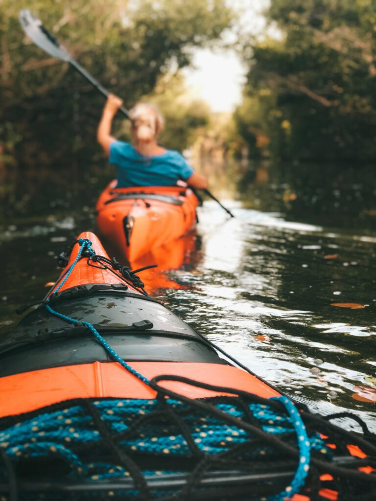 View from a kayak on the water with a person in a kayak in front paddling