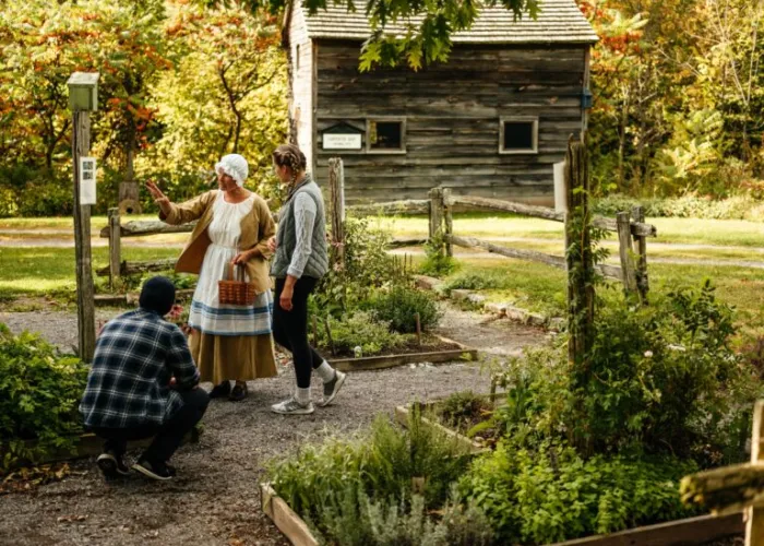 Two people interacting with a woman in historical clothing at the O'Hara Mill Homestead