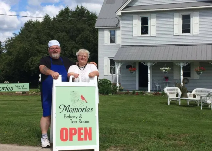 Two people standing by a OPEN sign in front of Memories Bakery and Tea Room