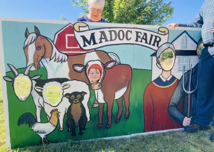 A young child smiling and putting their head through a fun sign at the Madoc Fair