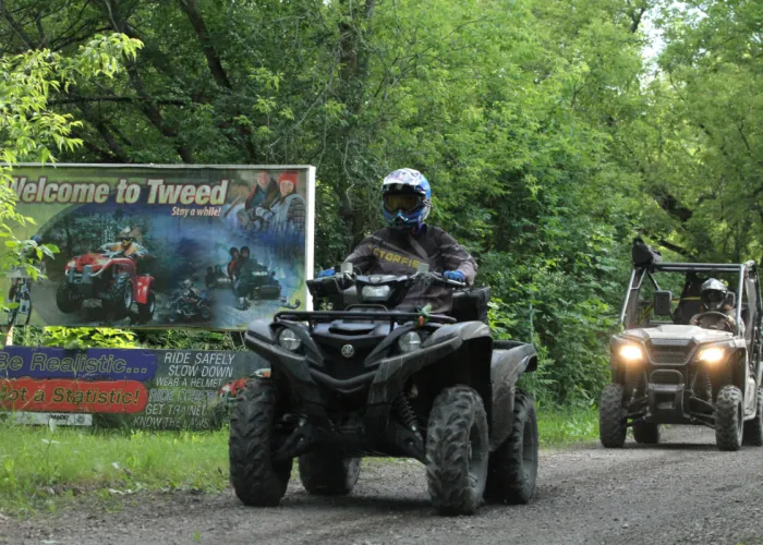 Person riding on an ATV along the EOTA Trail in Tweed, with Side-by-Side driving behind them