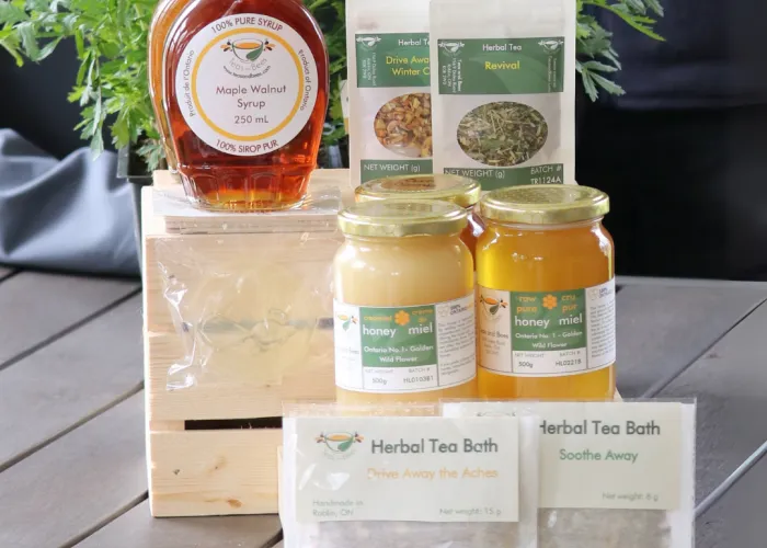 Teas and Bees products. Picture shows honey and tea products next to flowers on a gray table.