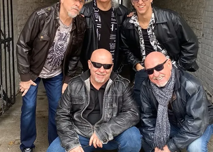 Five band members pose together in an alley with brick walls