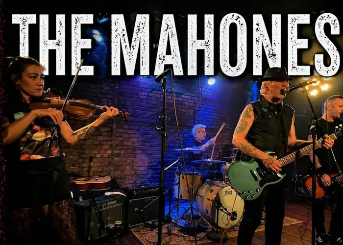 Photo of 4 band members on stage performing, name of band